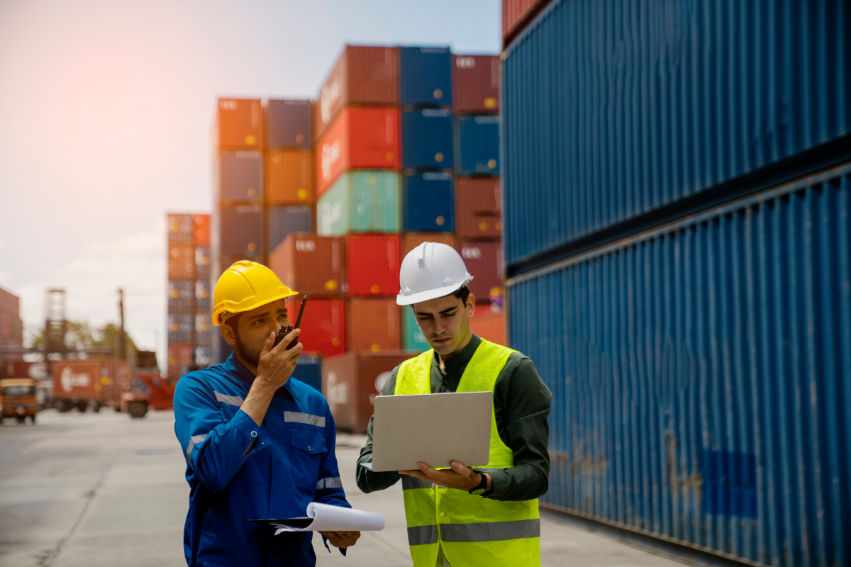 Two supply-chain auditors reviewing a container shipment with a laptop and clipboard at a port — Certainty Software